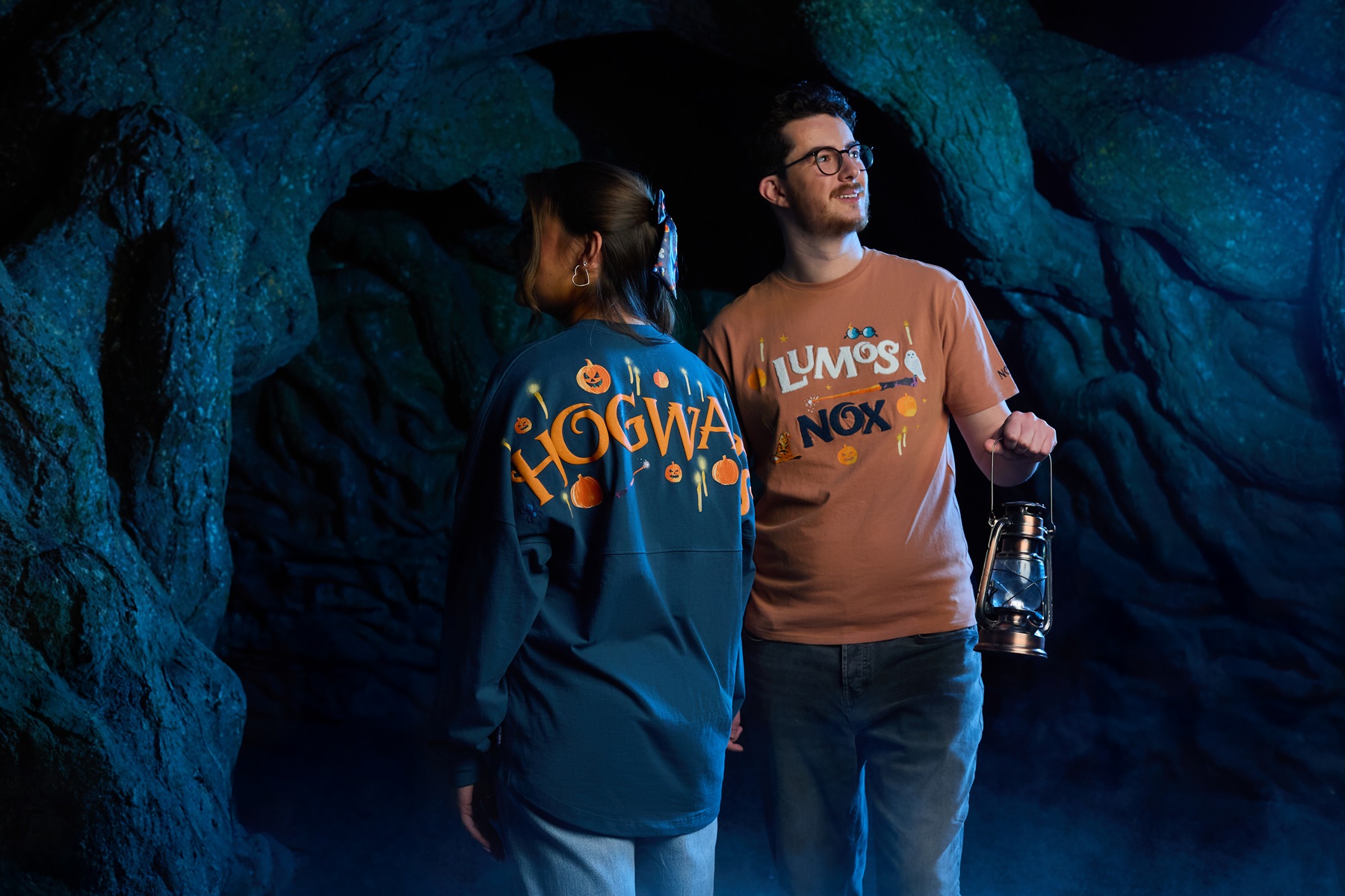 左圖：盧莫思・諾克斯Spirit Jersey長袖上衣，10,000日圓（含稅）。深海軍藍底色，正面印有立體感十足的「HOGWARTS」字樣，極具存在感。設計中融入南瓜燈、蠟燭與小蜘蛛，彷彿讓人置身萬聖節期間的大禮堂，帶來充滿秋意的奇幻氛圍。右圖：盧莫思・諾克斯T恤，3,000日圓（含稅）。設計靈感來自停駐在哈利魔杖上的海德威，搭配立體感「Lumos／Nox」字樣，袖口同樣印有咒語，整體散發出俏皮魔法氛圍。©東京華納兄弟